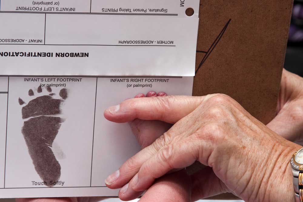 Hand holding a baby's inked foot to a birth certificate to make a foot print