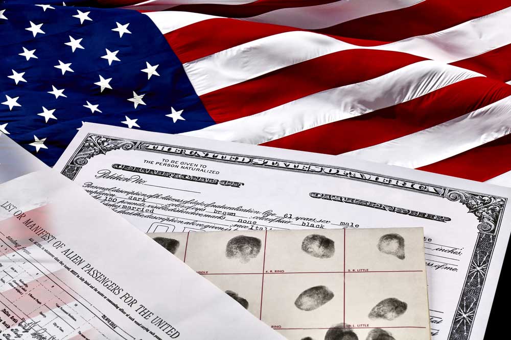 A birth certificate, finger print card, and passenger manifest laying on an American flag