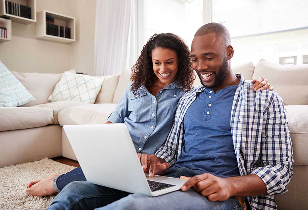 Man and woman sitting on living room floor looking at laptop screen