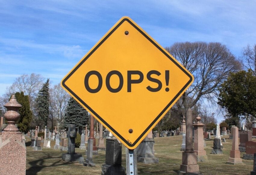 Yellow Street sign that says "Oops!" in front of a cemetary